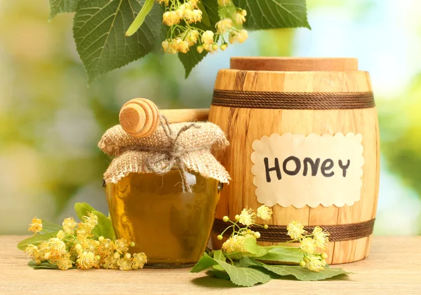 Vaso e botte con miele di tiglio e fiori su tavolo di legno su sfondo verde — Foto Stock