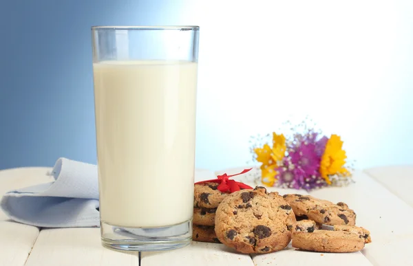 Стакан молока, шоколадное печенье с красной лентой и полевые цветы на деревянном столе на синем фоне — стоковое фото