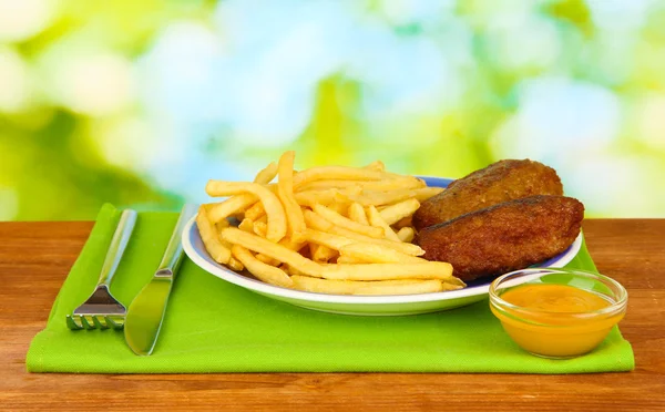 Potatis pommes frites med hamburgare på plattan på grön bakgrund närbild — Stockfoto
