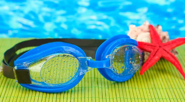 Blue swim goggles with drops on a bamboo pad, on blue sea background — Stock Photo, Image