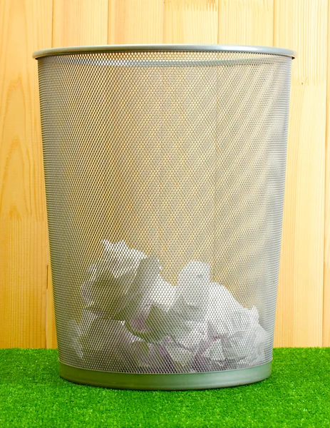 Cubo de basura de metal de papel sobre hierba sobre fondo de madera — Foto de Stock