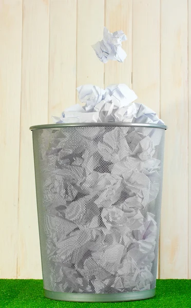 Металлический мусорный бак из бумаги на траве на деревянном фоне — стоковое фото