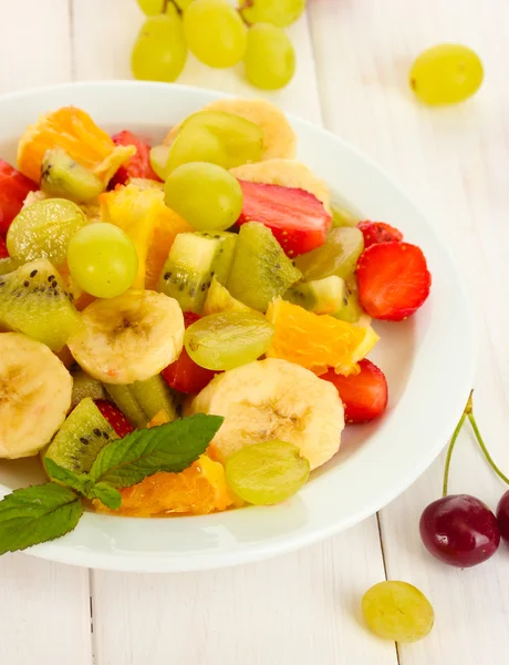 Obstsalat auf Teller und Beeren auf weißem Holztisch — Stockfoto