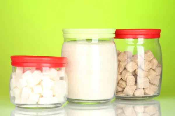 Frascos com caroço de açúcar de cana marrom, açúcar de cristal branco e açúcar de caroço branco no fundo colorido — Fotografia de Stock