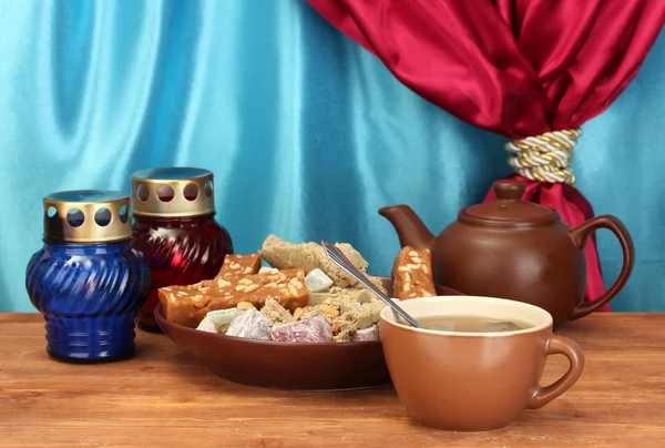 Bule com xícara e chapa com doces orientais - sherbet, halva e prazer turco em mesa de madeira em um fundo de close-up de cortina — Fotografia de Stock