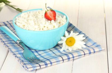 Cottage cheese with strawberry in blue bowl and fork on blue plaid napkin on white wooden table close-up clipart