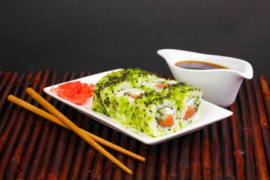 lezzetli rulo ile chopsticks bambu mat siyah arka plan üzerine beyaz tabakta servis