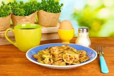 Fried zucchini with eggs and coffee for breakfast on wooden table on green background clipart