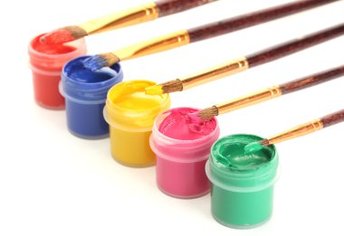 Brushes on the jars with colorful gouache on white background close-up