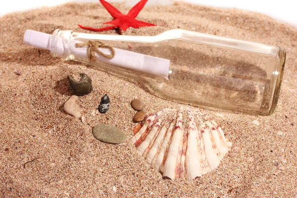 Glazen flesje met opmerking aan zand oever met schelpen — Stockfoto