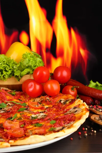 美味披萨、 意大利腊肠、 蔬菜和香料火焰背景上的木桌上 — 图库照片