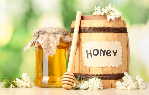 Miel dulce en barril y tarro con flores de acacia sobre mesa de madera sobre fondo verde —  Fotos de Stock