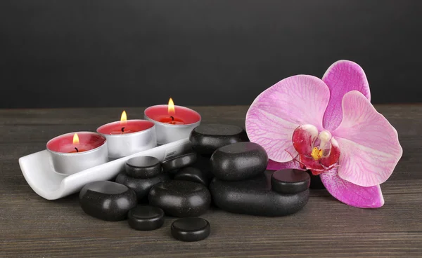 Piedras de spa con flor de orquídea y velas sobre mesa de madera sobre fondo gris —  Fotos de Stock