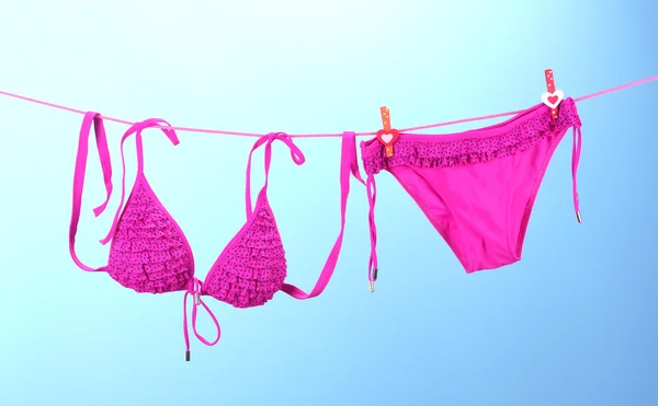 Women's swimsuit hanging on a rope on blue background — Stock Photo, Image