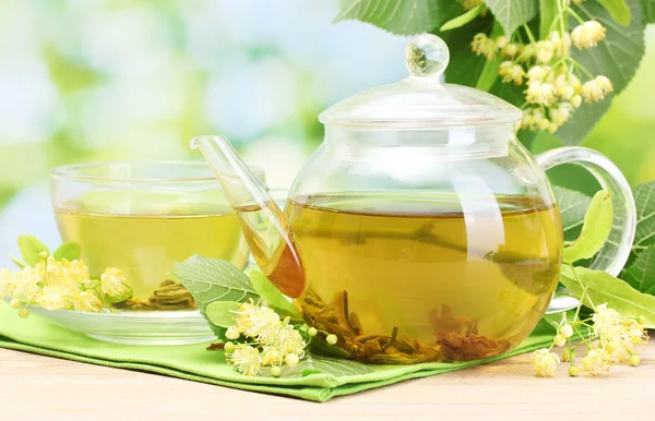 Tetera y taza con té de tilo y flores en la mesa de madera en el jardín — Foto de Stock