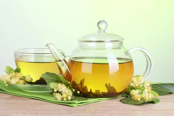 Bule e xícara com chá de tília e flores na mesa de madeira no fundo verde — Fotografia de Stock