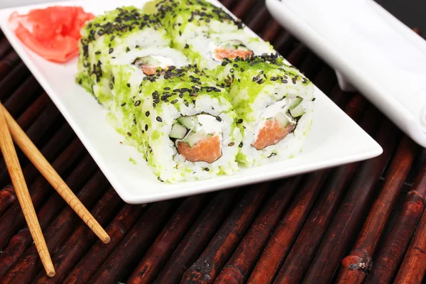 Tasty rolls served on white plate with chopsticks on bamboo mat close-up — Stock Photo, Image