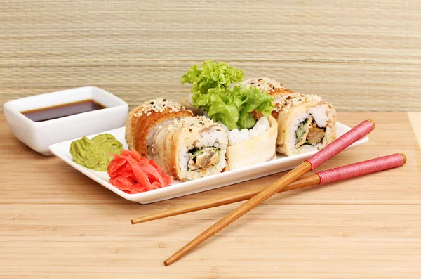 Lezzetli rulo ile chopsticks açık renkli ahşap tablo üzerinde beyaz tabakta servis — Stok fotoğraf