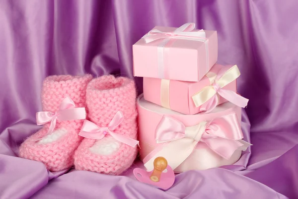 ピンクの赤ちゃんブーツ、おしゃぶり、絹の背景上のギフト — ストック写真