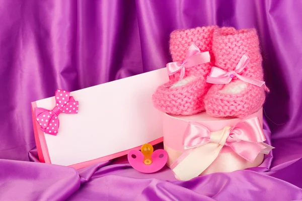 Rosa Babystiefel, Schnuller, Postkarte und Geschenke auf seidenem Hintergrund — Stockfoto