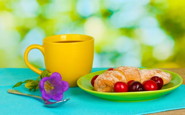 Croissant with cherries and coffee on wooden table on green background — Stock Photo, Image