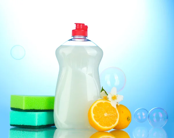 Dishwashing liquid with sponges and lemon with flowers on blue background — Stock Photo, Image