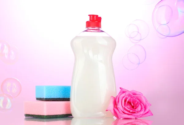 Dishwashing liquid with sponges and flower on pink background — Stock Photo, Image