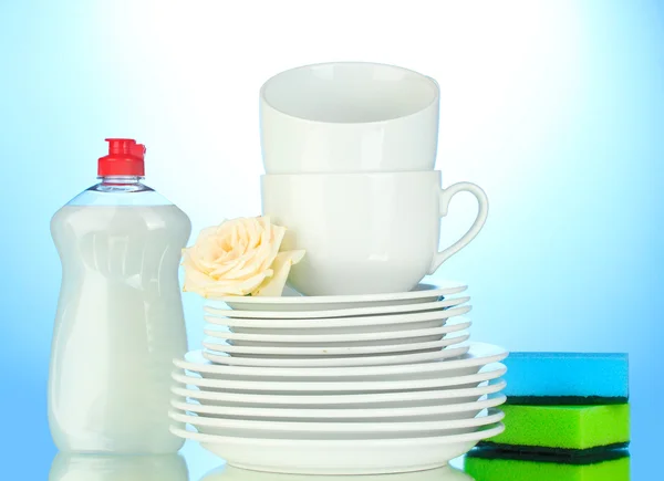 Pusty czyste talerze i kubki z płynu do mycia naczyń i gąbki na niebieskim tle — Zdjęcie stockowe