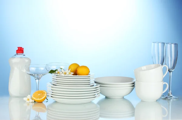 空のきれいな皿、グラス、カップ食器用液体と青色の背景にレモン — ストック写真