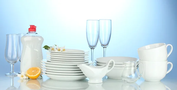 Piatti puliti vuoti, bicchieri e tazze con liquido per piatti e limone su sfondo blu — Foto Stock