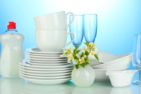 Пустые чистые тарелки, стаканы и чашки с жидкостью для мытья посуды и цветы на синем фоне — стоковое фото