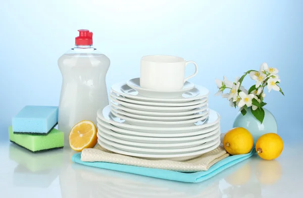 Пустые чистые тарелки и чашки с жидкостью для мытья посуды, губки и лимон на синем фоне — стоковое фото
