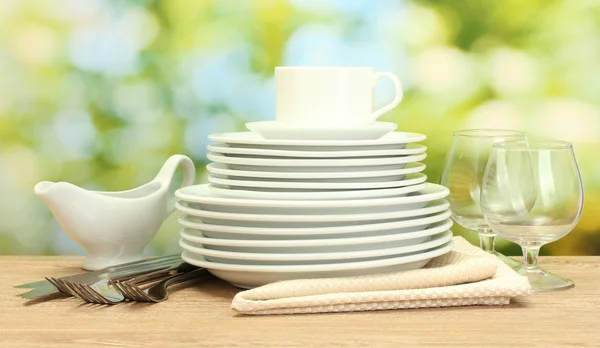 Empty clean plates, glasses and cup on wooden table on green background — Stock Photo, Image