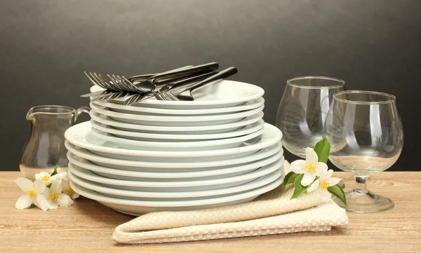Empty clean plates and glasses on wooden table on grey background — Stock Photo, Image