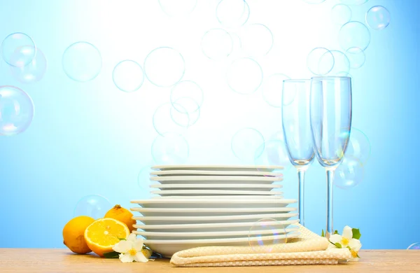 Platos y vasos limpios vacíos y limón sobre mesa de madera sobre fondo azul — Foto de Stock