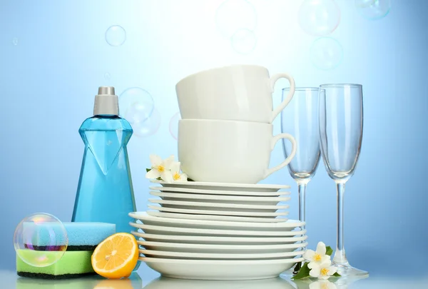 空のきれいな皿、グラス、洗剤、スポンジ、青い背景にレモンとカップ — ストック写真