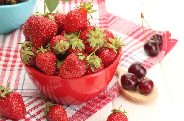 Ripe strawberries and cherry berries in bowls on white wooden table — Stock Photo, Image