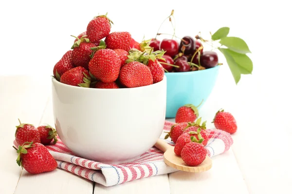 Mogna jordgubbar och körsbär bär i skålar på vita träbord — Stockfoto