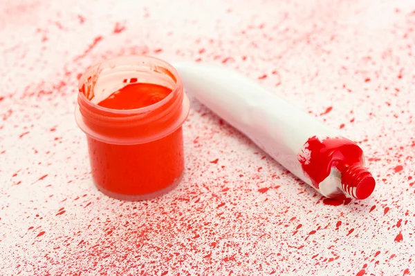 Pot avec gouache rouge et tube avec aquarelle rouge sur fond de spray rouge close-up — Photo