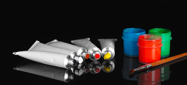 Tubes with colorful watercolors and jars with gouache and brush on black background close-up — Stock Photo, Image