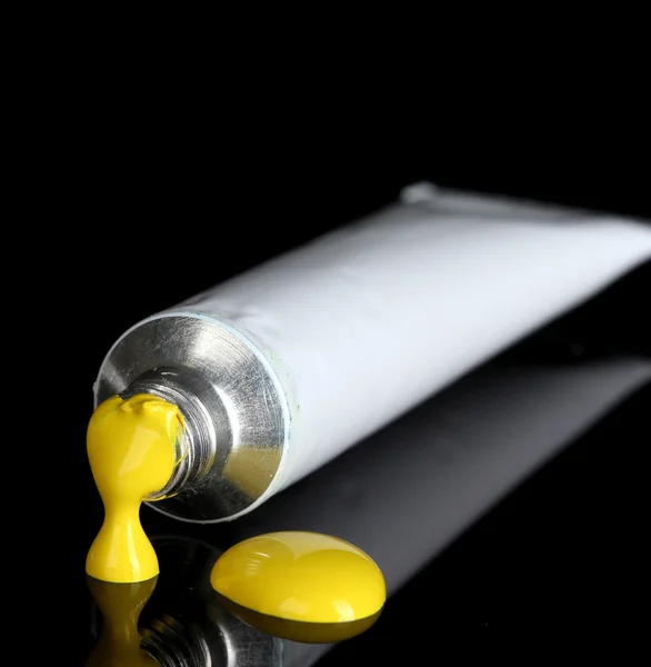Yellow paint follows from the tube on black background close-up — Stockfoto