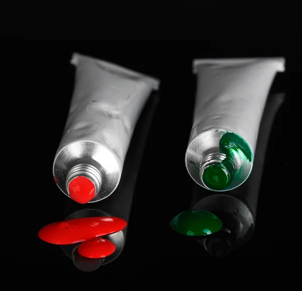 Червоні і зелені фарби випливають з трубок на чорному тлі крупним планом — стокове фото