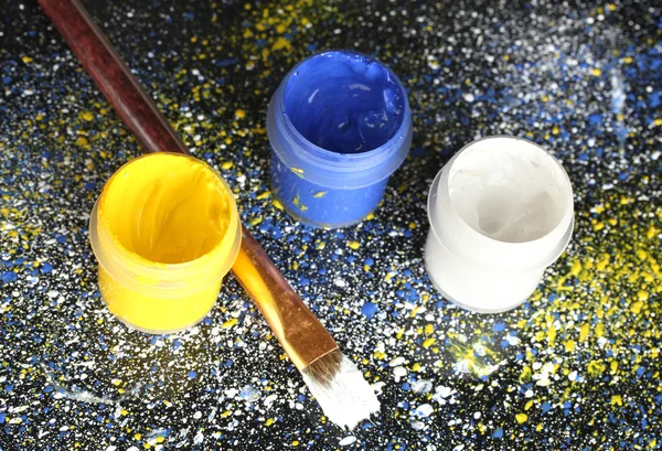 stock image Jars with colorful gouache and brush on black background, spattered with colorful paint close-up