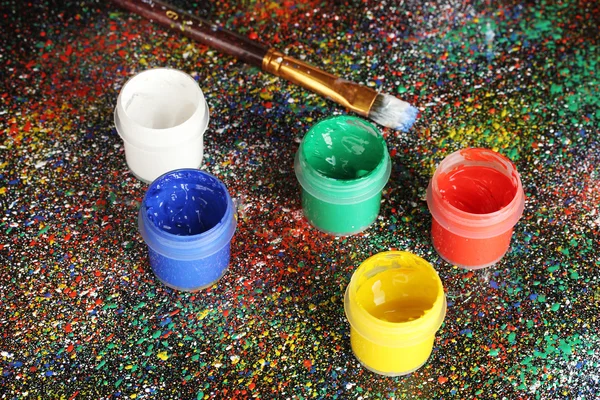 Frascos com guache colorido e escova sobre fundo preto, salpicados com pintura colorida close-up — Fotografia de Stock