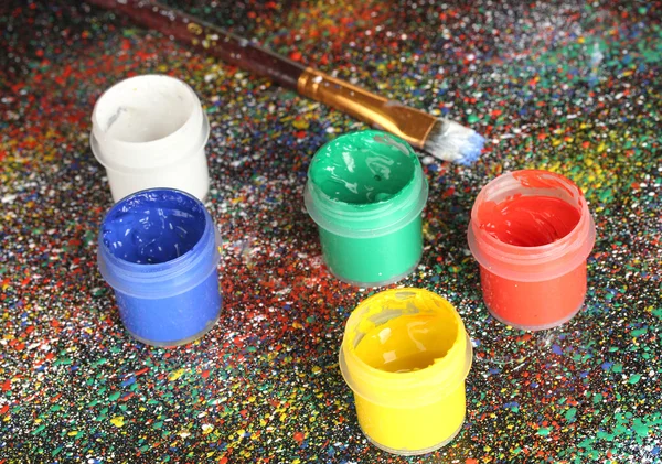 Jars with colorful gouache and brush on black background, spattered with colorful paint close-up — Stock Photo, Image