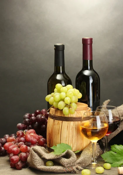 Barril, botellas y copas de vino y uvas maduras sobre mesa de madera sobre fondo gris — Foto de Stock