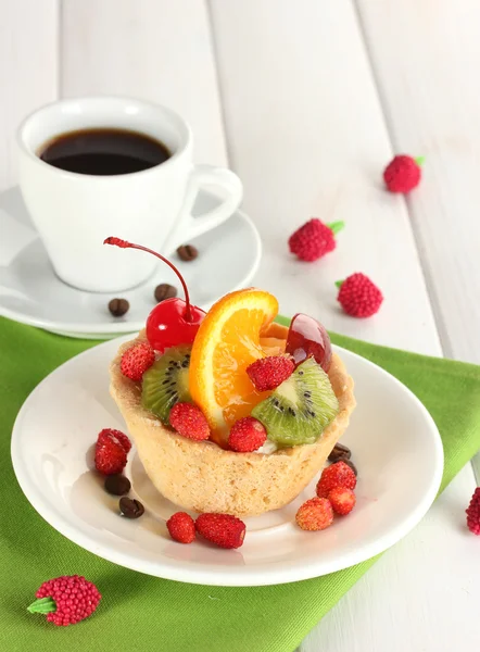 Zoete cake met vruchten op plaat en kopje koffie op houten tafel — Stockfoto