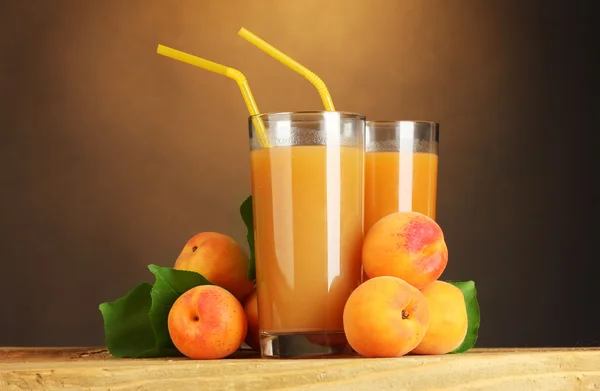 Glasses of apricot juice on wooden table on brown background — Stock Photo, Image