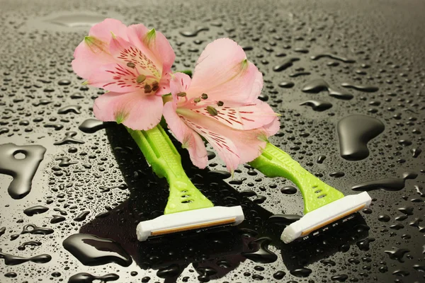 Afeitadoras de seguridad para mujer y flores con gotas sobre fondo gris — Foto de Stock