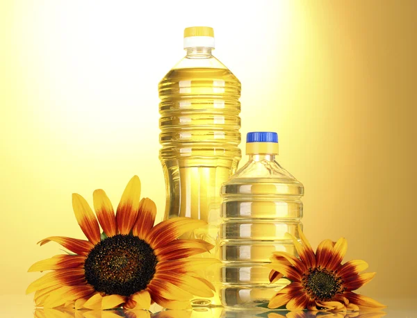 Подсолнечное масло и подсолнухи на желтом фоне — стоковое фото